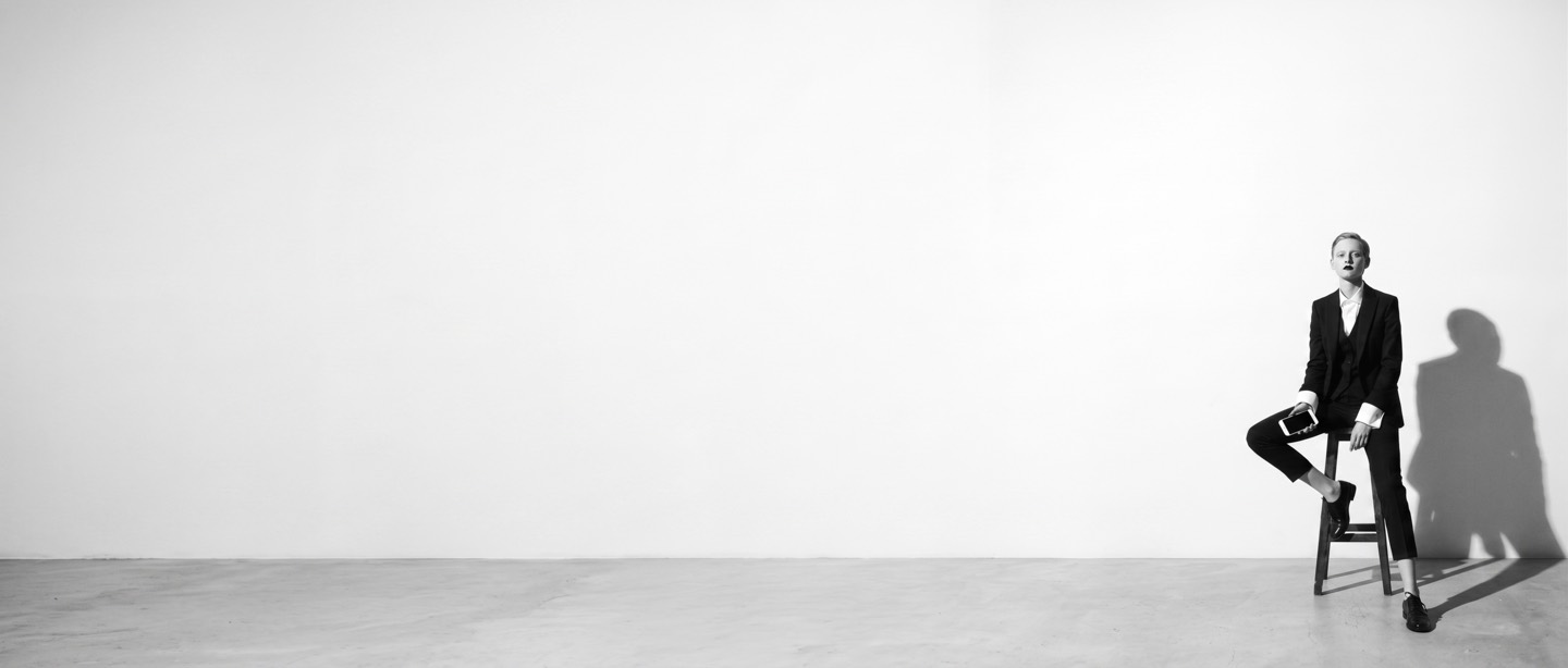 Fashion model in a tailored black suit, seated in a minimalist studio